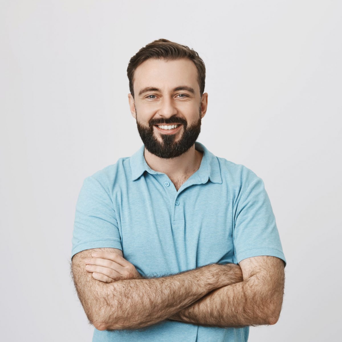 Portrait of a handsome bearded man smiling looking to the camera with his hands crossed isolated on white background. This person looks like an ordinary guy who is sincere and ready to help everyone. Portrait of a handsome bearded man smiling looking to the camera with his hands crossed isolated on white background. This person looks like an ordinary guy who is sincere and ready to help everyone who is in trouble.